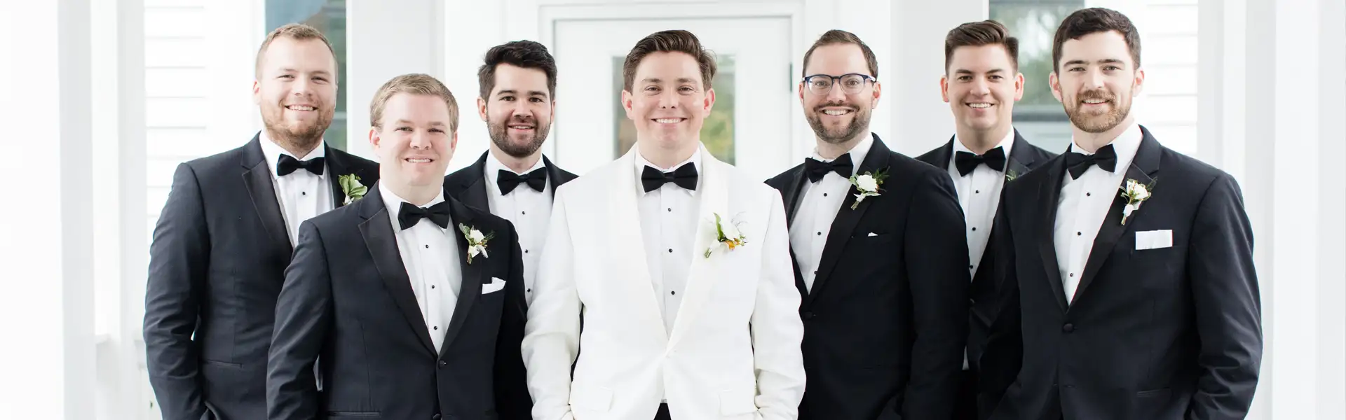 Groom in white tuxedo and out of town groomsmen in black tuxedos