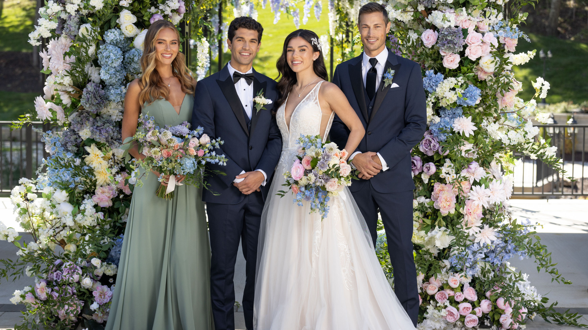 A groom and bride with friends taking a picture infront of the floral arch